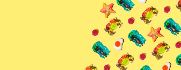 Sweet colorful assorted gummy candy on a yellow background. Jelly sweets. Minimal summer vacation...