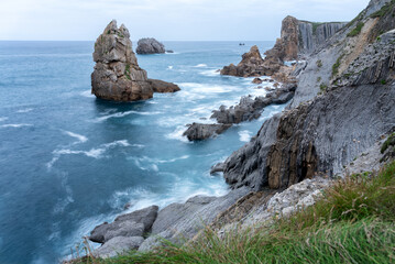 Long exposure view of a rocky shoreline with calm sea waters and rock formations under an overcast sky, Costa Quebrada, Urros de Liencres, Cantabria, Spain