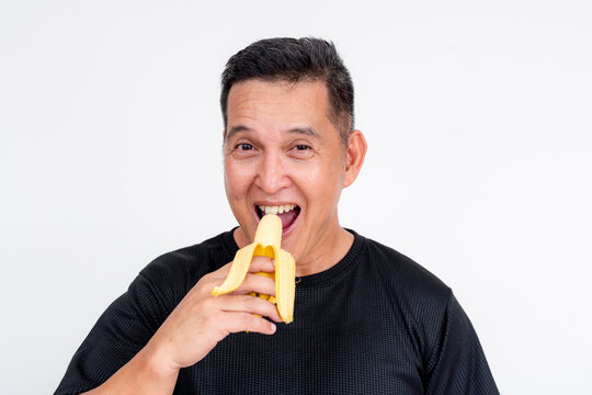 A cheerful middle-aged Asian man holding a peeled lakatan banana, ready to eat. Isolated on a white background.