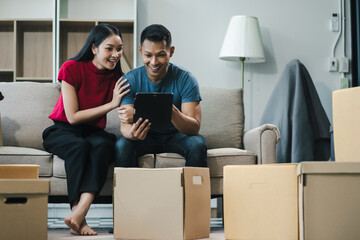 Young couple relaxing sitting on the sofa using the computer laptop around cardboard boxes, very...