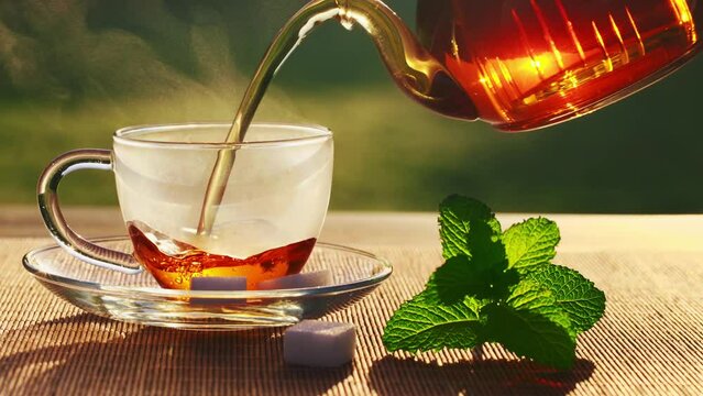 Pouring black tea into glass cup on wooden table