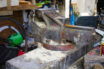 Old, sturdy bench vice on workbench in cluttered workshop, ready for heavy-duty tasks and...