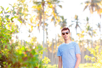 Portrait of a Brazilian man wearing sunglasses, looking at the camera. In the background, there are coconut trees, evoking a tropical and summer atmosphere