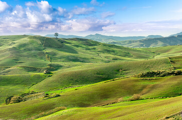 green spring season landscape of beautiful grassland hills in countryside with villages and mountains under scenic cloudy sky