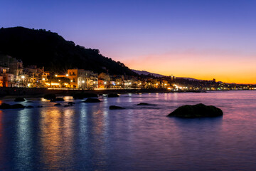 Fototapeta premium evening or night landscape of evening town coastline in golden lights and sea gulf with calm water and nice reflections with beautisul sunset sky on background