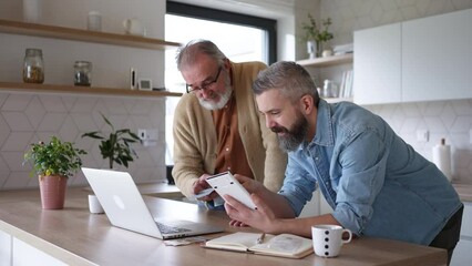 Mature son helping father to manage his finance, teaching how to work with internet baking and shopping online. Handsome son supporting dad, technology and digital literacy. - Powered by Adobe