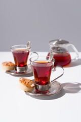 Dos tazas de té rojo con pasteles y dulces sobre mesa blanca y fondo gris