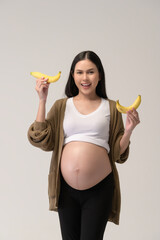 Portrait of Beautiful pregnant woman holding banana over white background studio, health and maternity concept.