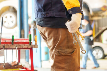 Mechanic holding wrenches, wearing white gloves and blue-yellow uniform. Close-up of lower body,...