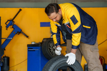 Mechanic working on tire, wearing white gloves and blue-yellow uniform. Focus on detailed tire...