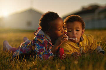 Nature, sunset and children blowing bubbles in park relaxing on grass together for bonding. Family,...
