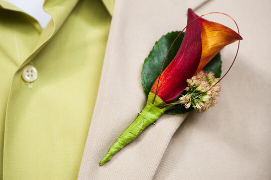 Closeup of a calla lily boutonniere worn on the lapel of a man in a tan suit