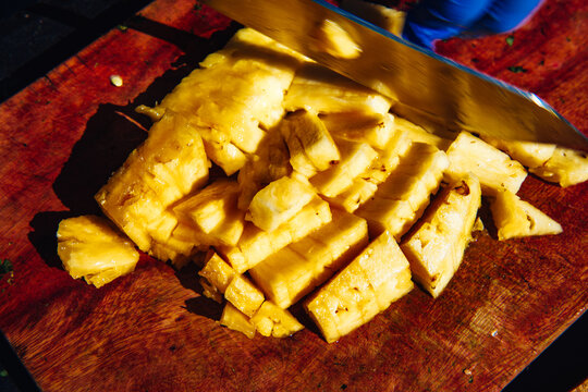 A knife cutting through slices of fresh pineapple on a wooden cutting surface, motion blur