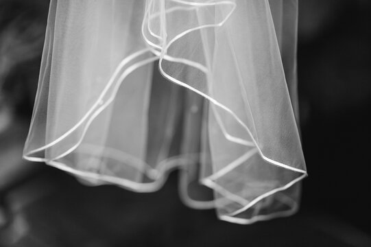 A black and white photo of the sheer bottom of a wedding dress hanging in a dark closet