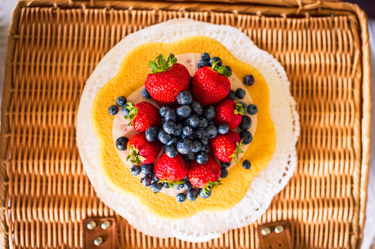 A colorful berry tart and white doily atop a wicker table, seen from above