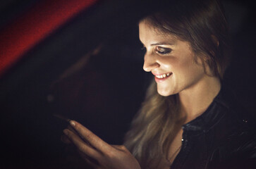 Naklejka premium Woman, smile and smartphone in car at night with transport for travel with technology for communication. Social media, reading or replying to text message with joke in New York with tnc or taxi.