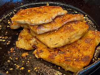Vegan seitan schitzel slices frying in cast iron pan, cut steak style