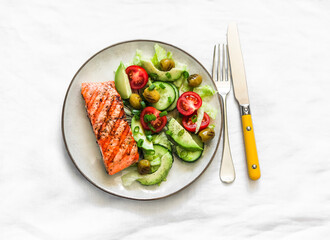 Healthy delicious lunch, dinner - grilled salmon and avocado, cherry tomatoes, cucumber, olives, iceberg lettuce on a light background, top view