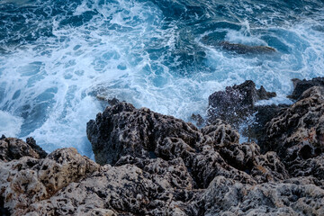 Beautiful view of water crashing on the rocky shore. Wave splashing against stones on shore close up.