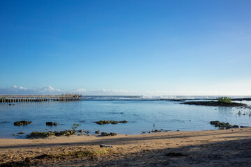 Serene view of a wooden pier extending into the calm waters at Cloud 9, Philippines. The bright blue sky and clear waters create a peaceful and inviting atmosphere.