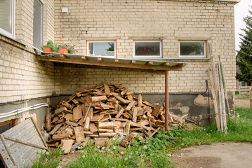 big pile of firewood in the yard under the roof of the house