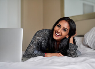 Indian woman, bed and happy on portrait with laptop in home for browsing internet, streaming service or entertainment. Female person, bedroom and happy on website for online booking or applications