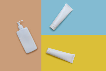 White containers for cream and lotion on colored paper backgrounds.