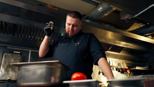 in professional kitchen in a chef in a black jacket pours oil into vegetables in an iron bowl
