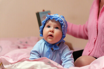 Sweet baby with a blue bonnet peacefully on a soft pink blanket.