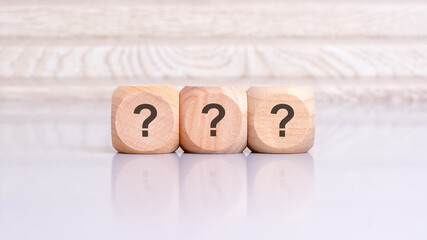 three wooden blocks with question marks over a gray background with copy space