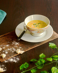 Creamy vegetable soup bowl on a coffee table with breadcrumbs, serviette cloth piece and green leaves