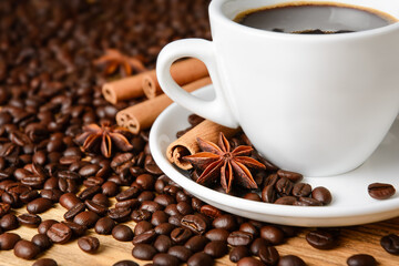 Coffee cup, coffee beans, cinnamon sticks and star anise on wooden table, close-up