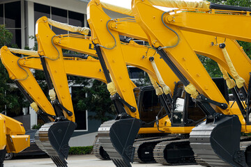 A row of yellow construction machines are parked in a lot. The machines are all different sizes and...