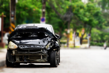 A black car with a smashed front end is parked on the side of the road. The car appears to have...