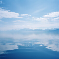 A calm lake with mountains and white clouds in the distance