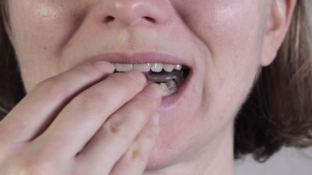 Woman puts Soft mouth guard for TMJ, TMD in her mouth. Teeth protection. Dental guard. TMJ disorder. Pain in jaw. Teeth grinding.