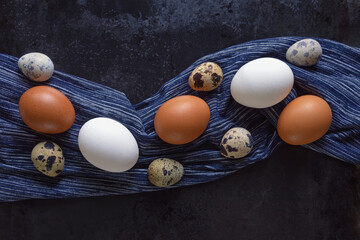 White and brown chicken eggs and quail eggs on dark metal table