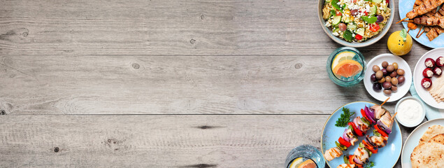 Summer Mediterranean theme food side border. Top down view on a wood banner background with copy space. Grilled skewers, salads, snacks, pita and tzatziki.