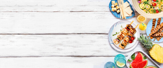 Summer food side border with  meat skewers, salad, fruit and snacks. Above view on a white wood banner background. Copy space.