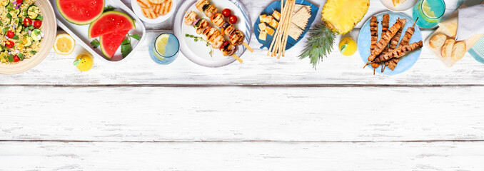 Summer food top border with  meat skewers, salad, fruit and snacks. Overhead view on a white wood...