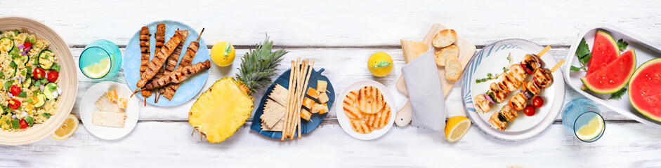 Summer food table scene with  meat skewers, salad, fruit and snacks. Top view on a white wood...