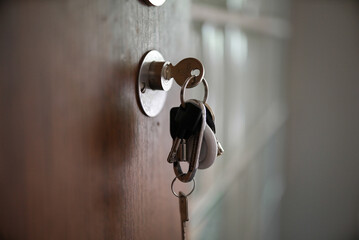 Keys hanging from a keyhole in a wooden door. This close-up shot highlights the everyday practicality and security aspect of home life, emphasizing the importance of keys and access.