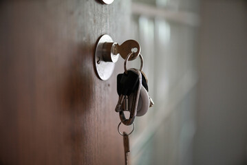 Keys hanging from a keyhole in a wooden door. This close-up shot highlights the everyday...
