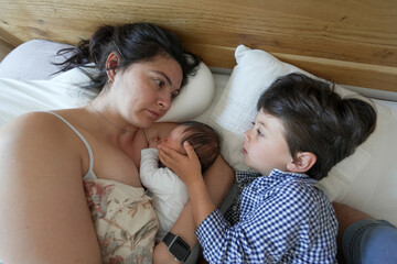 Mother breastfeeding newborn baby while older child lovingly holds the baby's head, family togetherness, cozy setting, capturing maternal affection and sibling bonding, tranquil environment