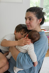 Smiling mother holding baby while engaging with older child at the table, demonstrating the warmth...