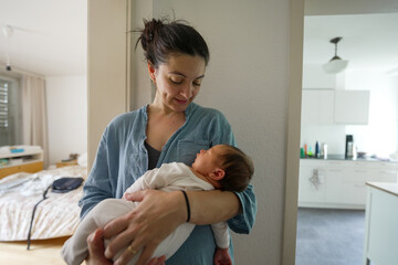 Mother lovingly holding her newborn, gazing down with a warm smile. This intimate scene captures...