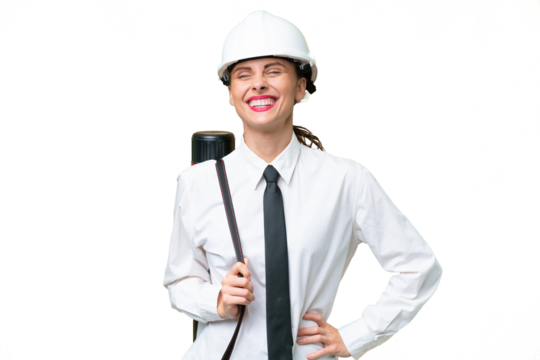 Young architect woman with helmet and holding blueprints over isolated background posing with arms at hip and smiling