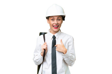 Young architect woman with helmet and holding blueprints over isolated background with surprise facial expression