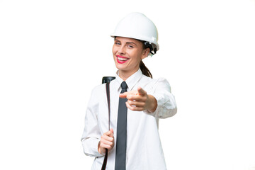 Young architect woman with helmet and holding blueprints over isolated background pointing front with happy expression