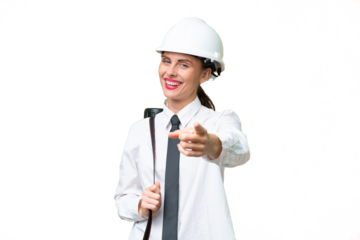 Young architect woman with helmet and holding blueprints over isolated background pointing front with happy expression